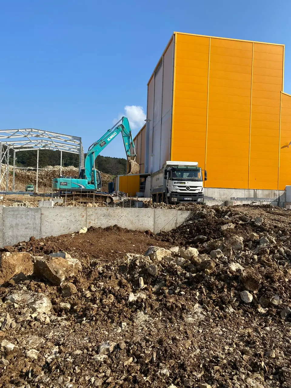 Fabrika sahasında ekskavatör damperli kamyona hafriyat yüklüyor